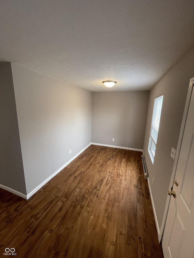 empty room featuring baseboards, dark wood finished floors, a textured ceiling, and baseboard heating