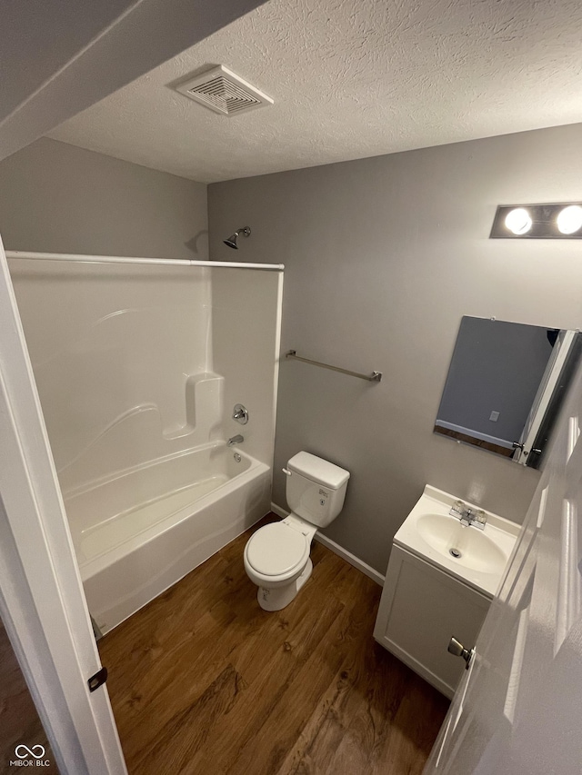 full bathroom featuring a textured ceiling, toilet, wood finished floors, vanity, and visible vents