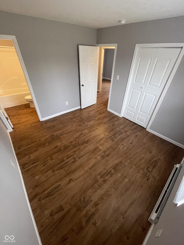 unfurnished bedroom featuring ensuite bathroom, dark wood finished floors, and baseboards