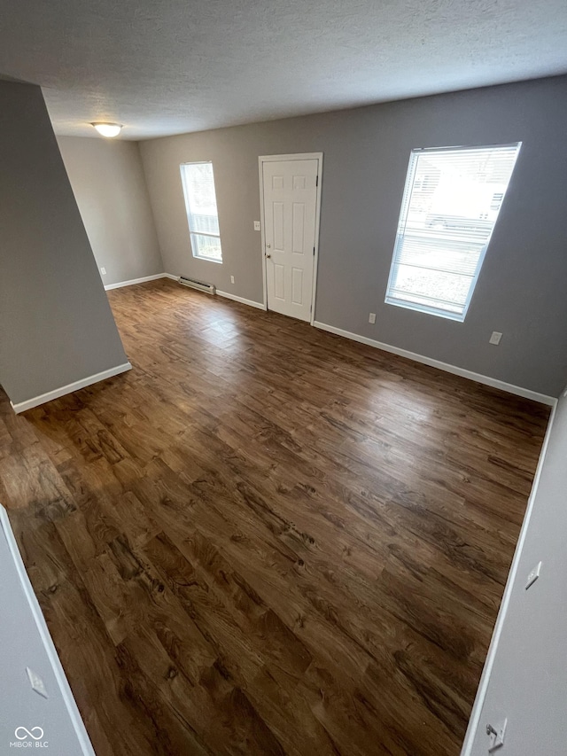 interior space featuring a baseboard heating unit, baseboards, dark wood-type flooring, and a textured ceiling