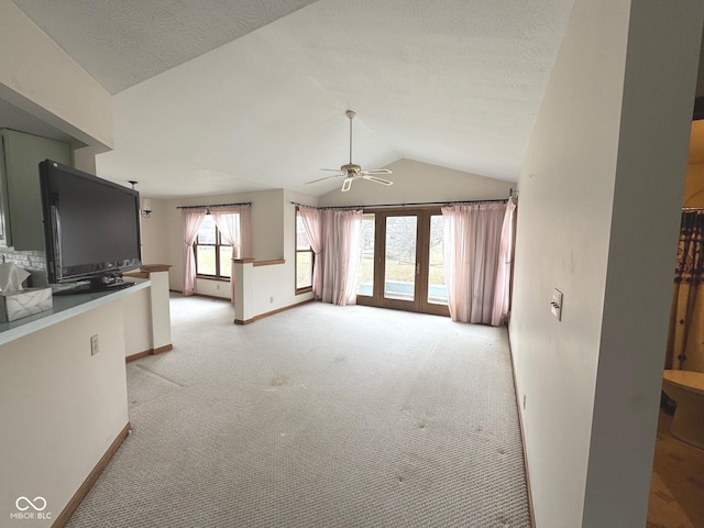 unfurnished living room featuring french doors, light colored carpet, vaulted ceiling, a textured ceiling, and ceiling fan