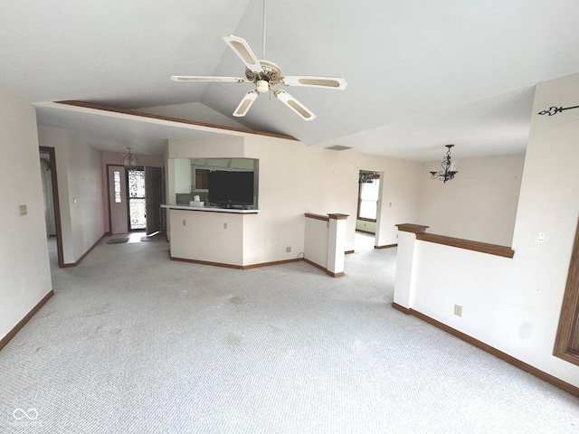 unfurnished living room featuring ceiling fan with notable chandelier, vaulted ceiling, light colored carpet, and a healthy amount of sunlight