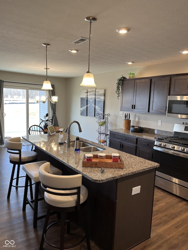 kitchen with sink, stainless steel appliances, light stone countertops, an island with sink, and decorative light fixtures