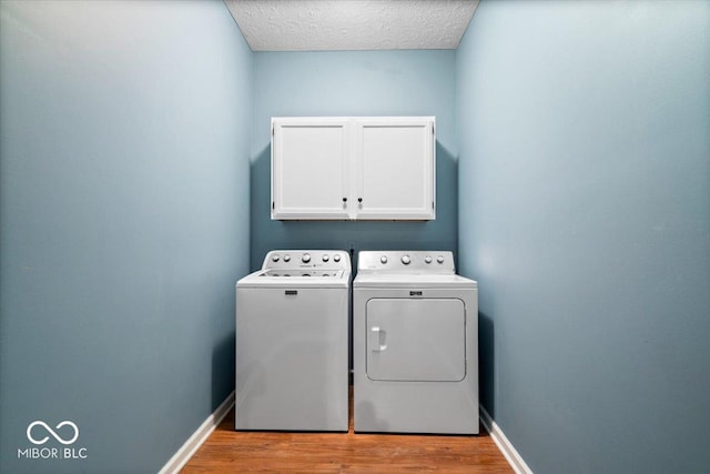 laundry room with separate washer and dryer, light hardwood / wood-style flooring, cabinets, and a textured ceiling