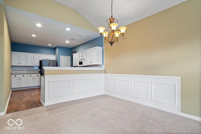 kitchen with vaulted ceiling, white cabinetry, stainless steel fridge, hanging light fixtures, and kitchen peninsula