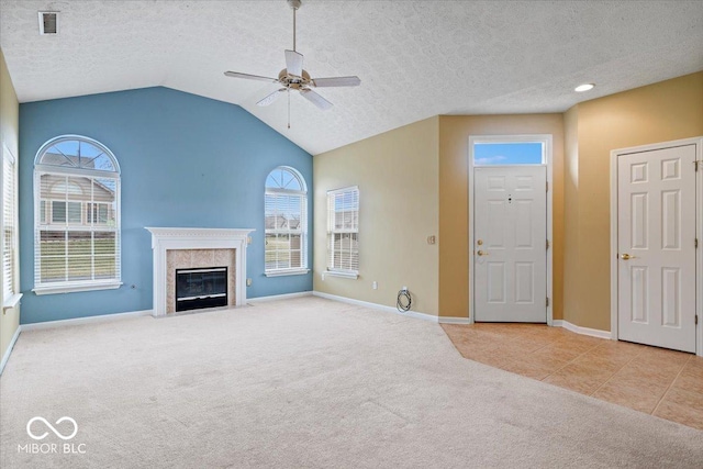 unfurnished living room featuring lofted ceiling, ceiling fan, a high end fireplace, a textured ceiling, and light carpet