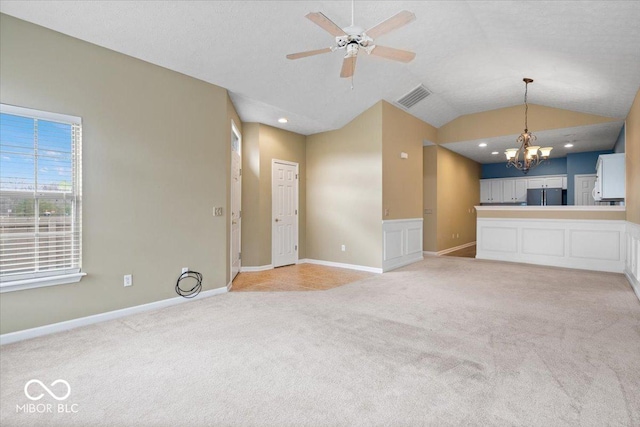 unfurnished living room with lofted ceiling, ceiling fan with notable chandelier, and light carpet