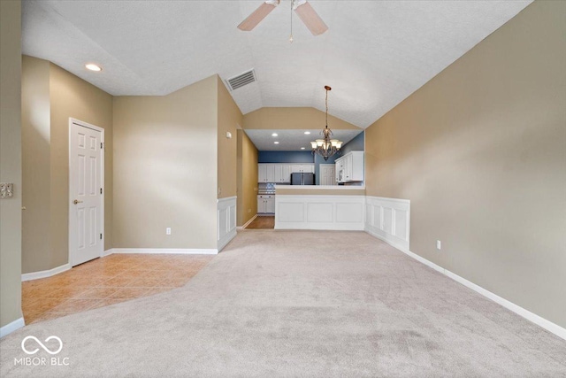 unfurnished living room with light carpet, ceiling fan with notable chandelier, vaulted ceiling, and a textured ceiling