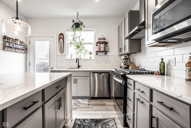 kitchen with appliances with stainless steel finishes, sink, wall chimney range hood, and gray cabinetry