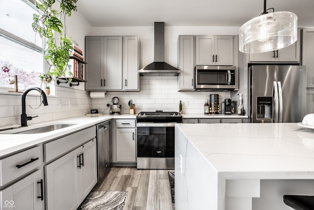 kitchen featuring sink, gray cabinets, appliances with stainless steel finishes, light stone counters, and wall chimney exhaust hood