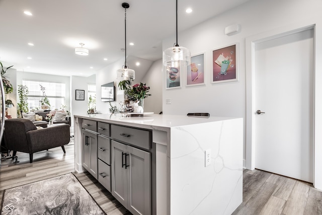 kitchen featuring decorative light fixtures, gray cabinets, light hardwood / wood-style floors, and light stone countertops