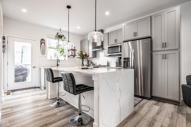 kitchen featuring gray cabinetry, light stone counters, decorative light fixtures, a center island, and appliances with stainless steel finishes