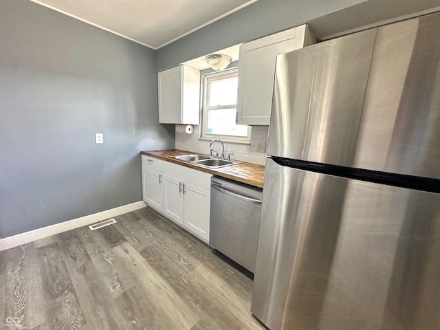 kitchen featuring stainless steel appliances, butcher block counters, sink, and white cabinets