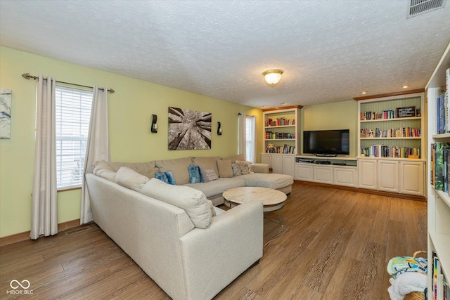 living room with hardwood / wood-style flooring, built in features, and a textured ceiling