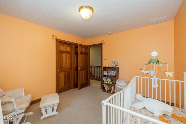 bedroom featuring a nursery area, carpet, and a textured ceiling