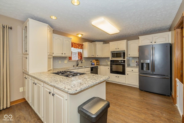 kitchen with sink, hardwood / wood-style floors, light stone counters, black appliances, and kitchen peninsula