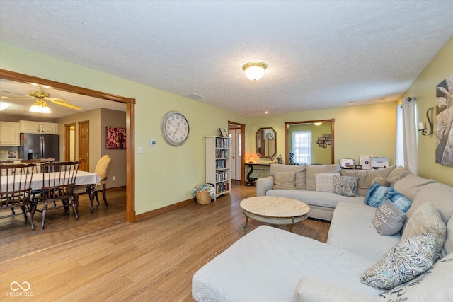 living room featuring ceiling fan, a textured ceiling, and light hardwood / wood-style floors