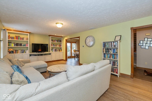 living room with built in shelves, light hardwood / wood-style floors, and a textured ceiling