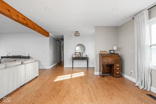 unfurnished living room featuring beamed ceiling and light wood-type flooring