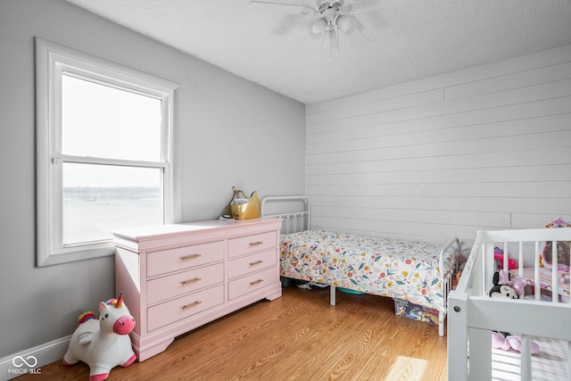 bedroom featuring ceiling fan, light hardwood / wood-style flooring, wooden walls, and a textured ceiling