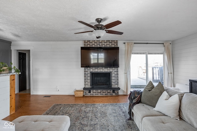 living room with hardwood / wood-style flooring, ceiling fan, a brick fireplace, and a textured ceiling