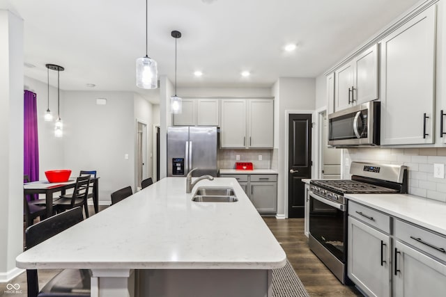 kitchen featuring appliances with stainless steel finishes, decorative light fixtures, sink, and a center island with sink