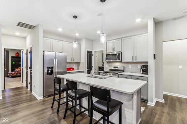 kitchen with an island with sink, stainless steel appliances, sink, and hanging light fixtures