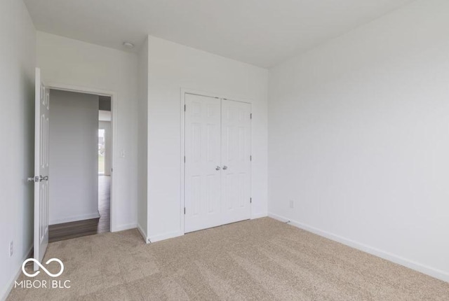 unfurnished bedroom with a closet, light carpet, and baseboards