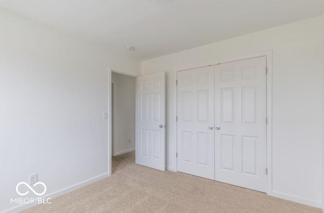 unfurnished bedroom featuring baseboards, a closet, and light colored carpet