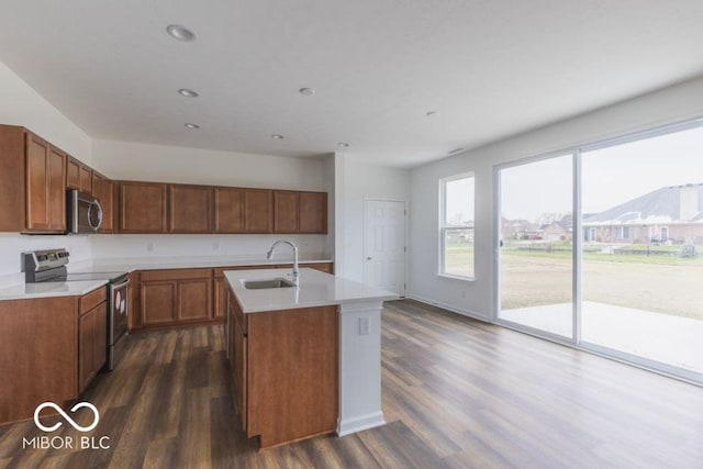 kitchen with a kitchen island with sink, a sink, light countertops, appliances with stainless steel finishes, and brown cabinets