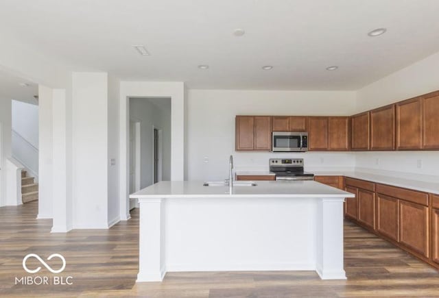 kitchen with brown cabinets, a center island with sink, appliances with stainless steel finishes, and light countertops