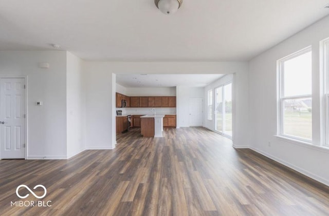 unfurnished living room featuring a sink, baseboards, and dark wood-style flooring