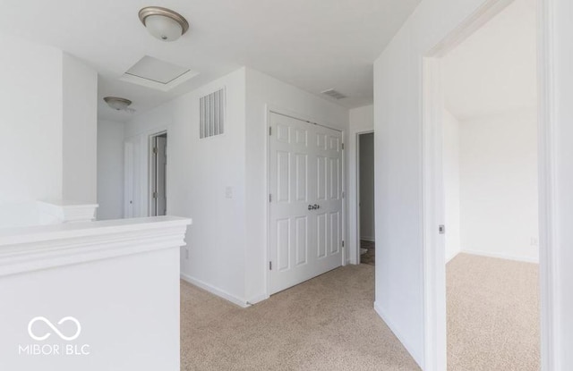 corridor with attic access, light carpet, visible vents, and baseboards