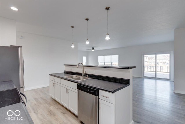 kitchen featuring appliances with stainless steel finishes, sink, white cabinets, hanging light fixtures, and a kitchen island with sink