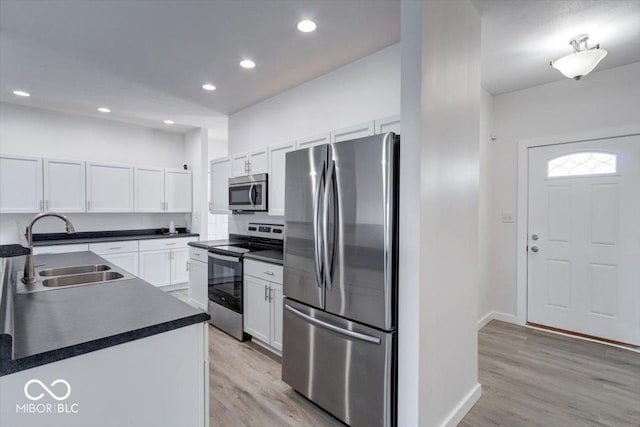 kitchen with appliances with stainless steel finishes, sink, white cabinets, and light hardwood / wood-style flooring