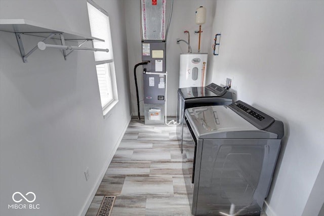 clothes washing area with water heater, washing machine and clothes dryer, and light wood-type flooring