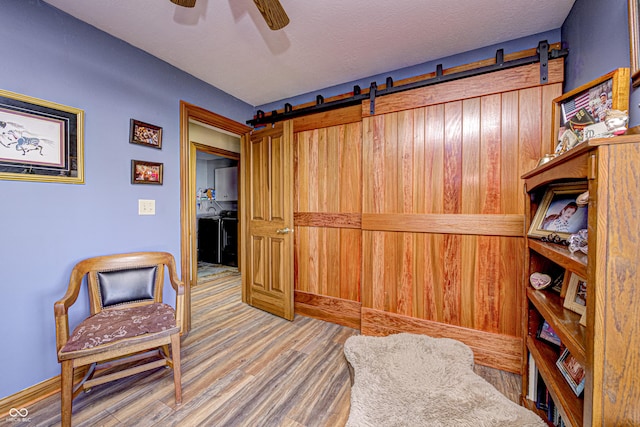 living area with ceiling fan, a barn door, a textured ceiling, and hardwood / wood-style floors