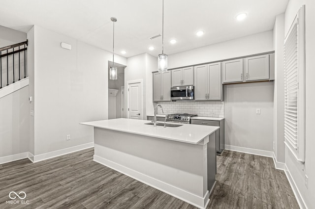 kitchen featuring stainless steel appliances, light countertops, hanging light fixtures, a kitchen island with sink, and a sink