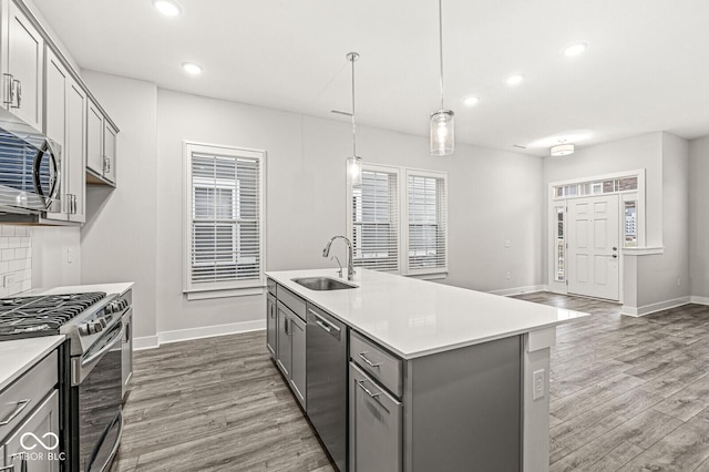 kitchen featuring stainless steel appliances, light countertops, a sink, and a center island with sink