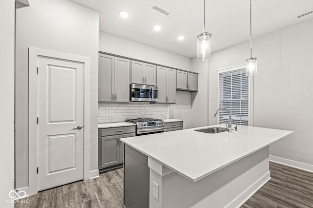kitchen featuring stainless steel appliances, light countertops, a center island with sink, and decorative light fixtures
