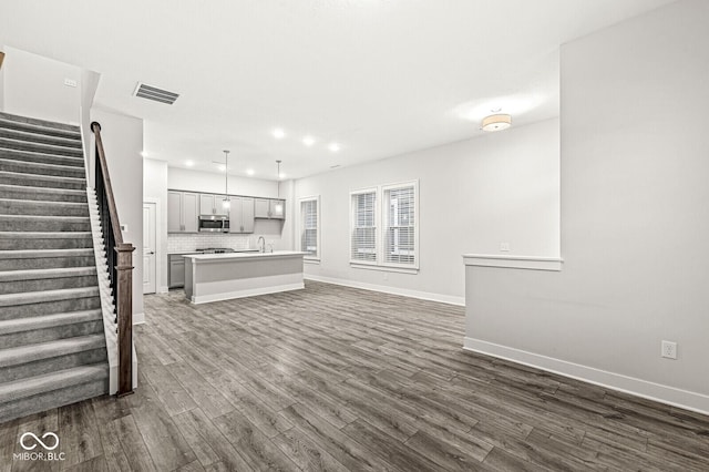 unfurnished living room with stairs, dark wood-style flooring, visible vents, and baseboards