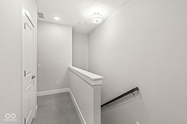 hallway with visible vents, dark carpet, an upstairs landing, and baseboards