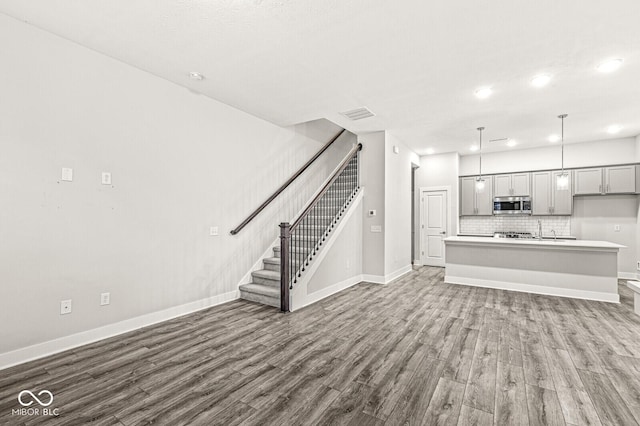 unfurnished living room featuring dark wood-style floors, visible vents, baseboards, and stairs