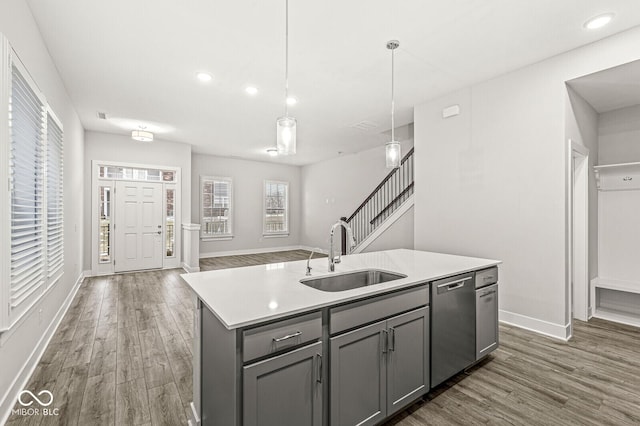 kitchen with a sink, light countertops, hanging light fixtures, dishwasher, and a center island with sink