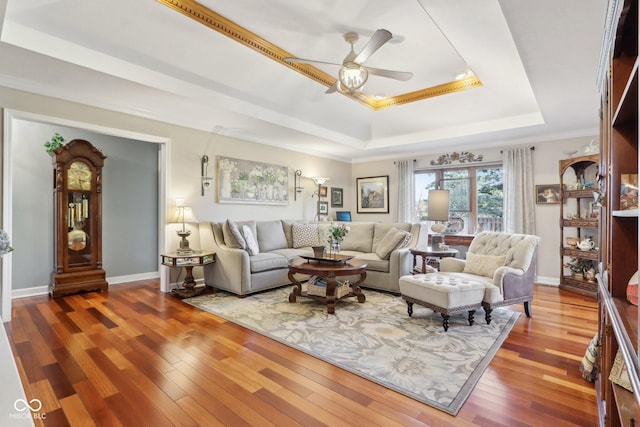 living room featuring a tray ceiling, wood-type flooring, ornamental molding, and ceiling fan