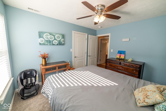 carpeted bedroom featuring multiple windows, a textured ceiling, and ceiling fan