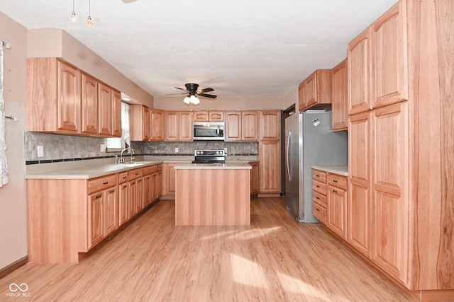 kitchen with light brown cabinetry, a sink, a kitchen island, stainless steel appliances, and ceiling fan