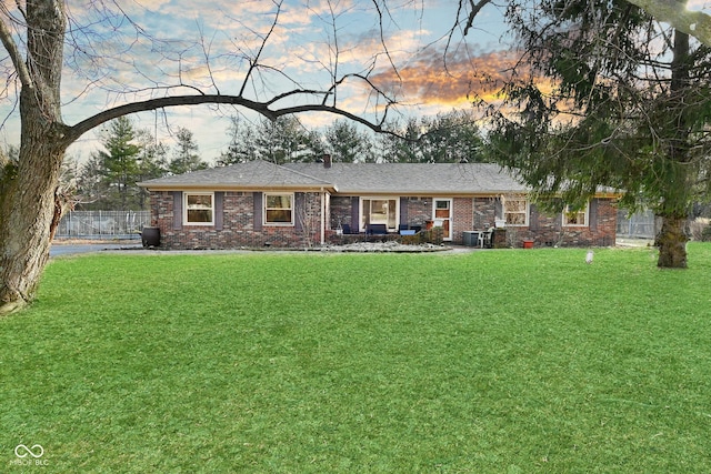 ranch-style home featuring brick siding, a chimney, a front yard, and fence