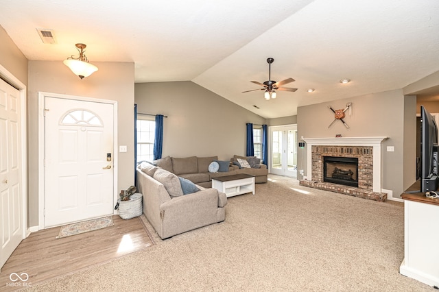 living room with ceiling fan, lofted ceiling, a brick fireplace, and light wood-type flooring