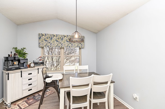 dining space featuring hardwood / wood-style floors, vaulted ceiling, and a textured ceiling